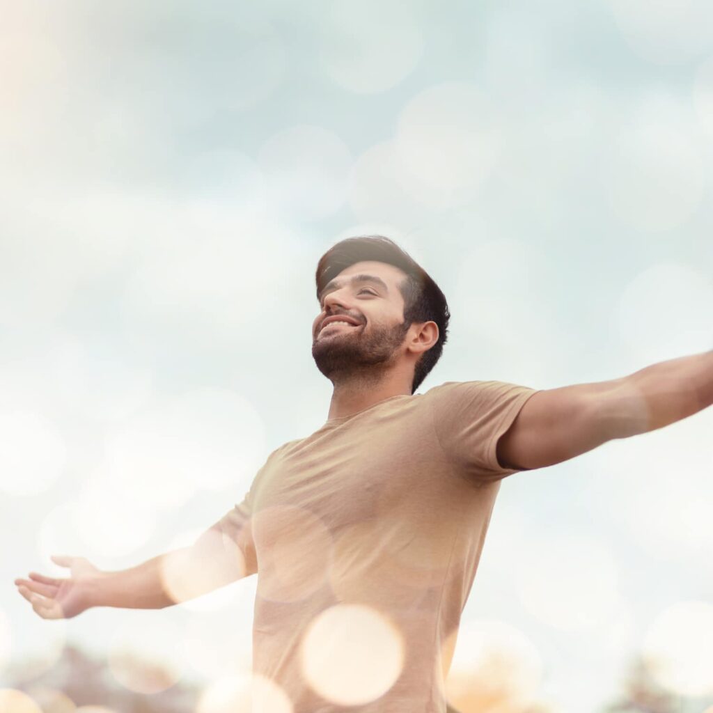 man with beard with arms outstretched in sunlight showing how wellness services in Benton County has helped him find joy.